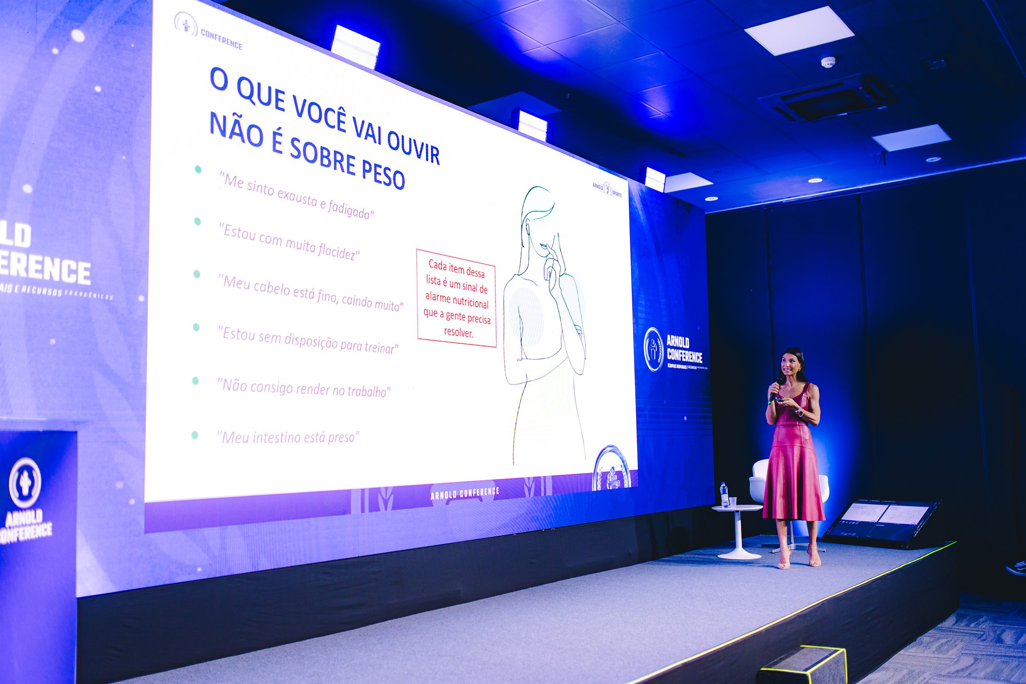 Alessandra palestrando ao lado de uma apresentação sobre saúde feminina